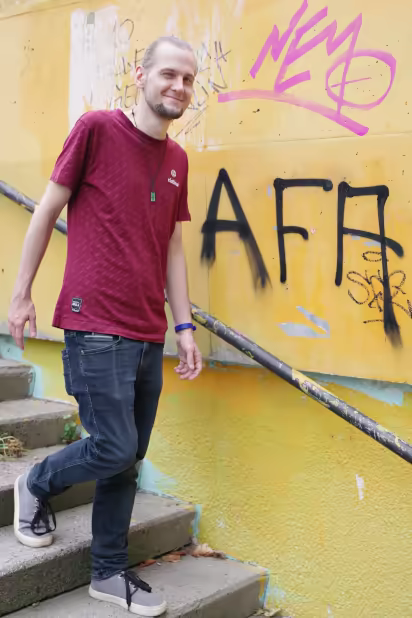 ich, lächelnd mit zusammengebundenen Haaren, eine Treppe herunterlaufend, im Hintergrund an einer Wand steht 